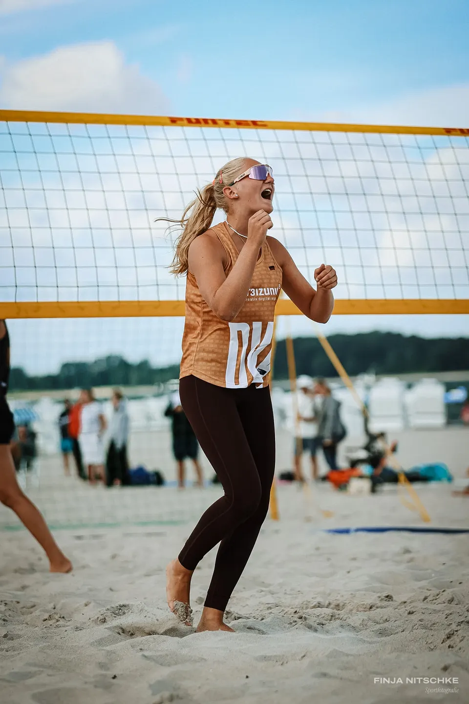 Beach volleyball player cheering with clenched fists in front of the yellow net