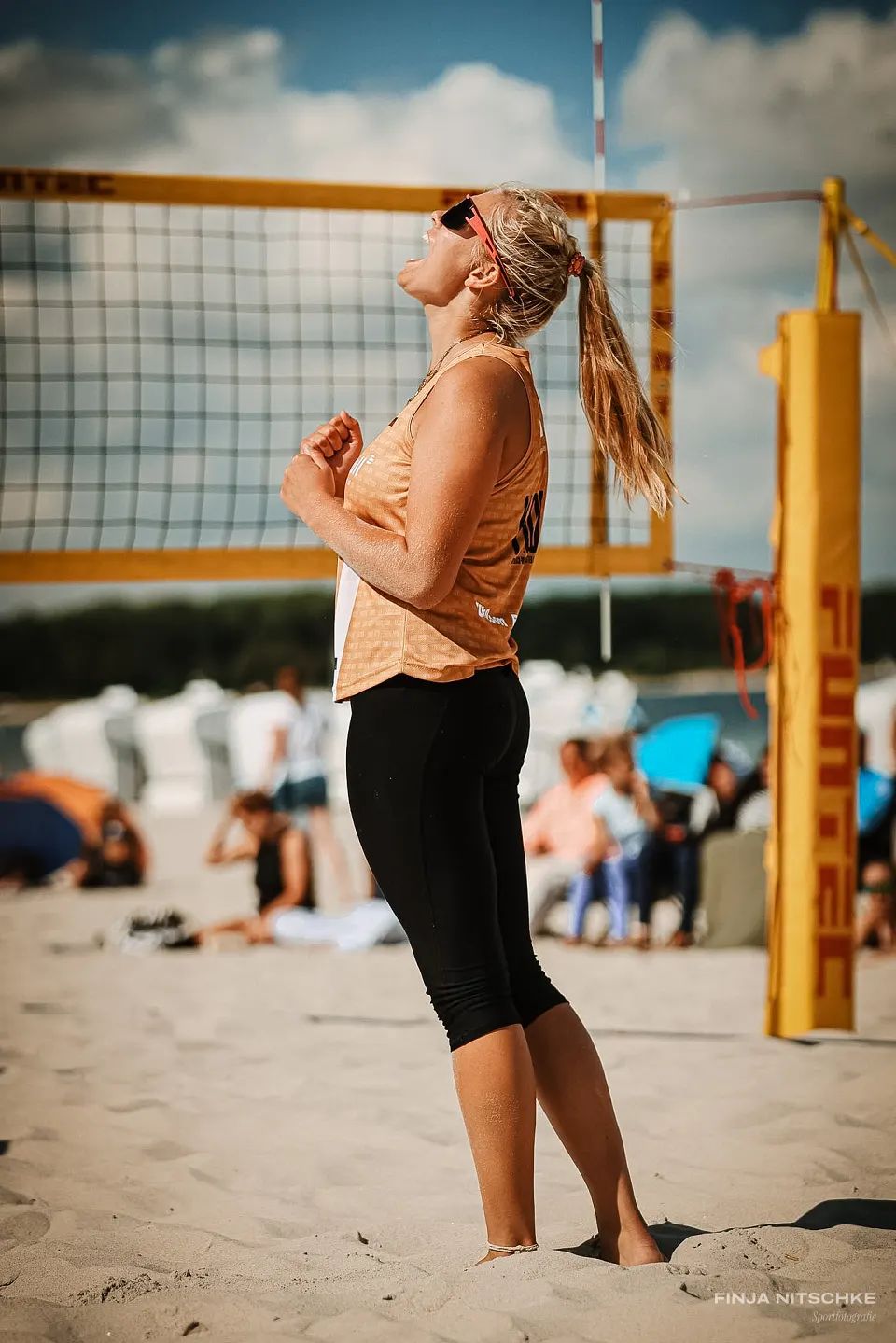 Beach volleyball player celebrating with clenched fists, head thrown back at the net