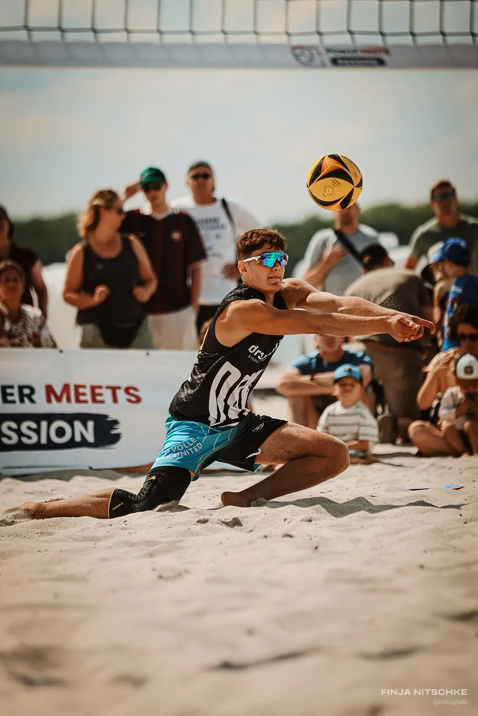Beachvolleyballer baggert im tiefen Ausfallschritt vor dem Publikum