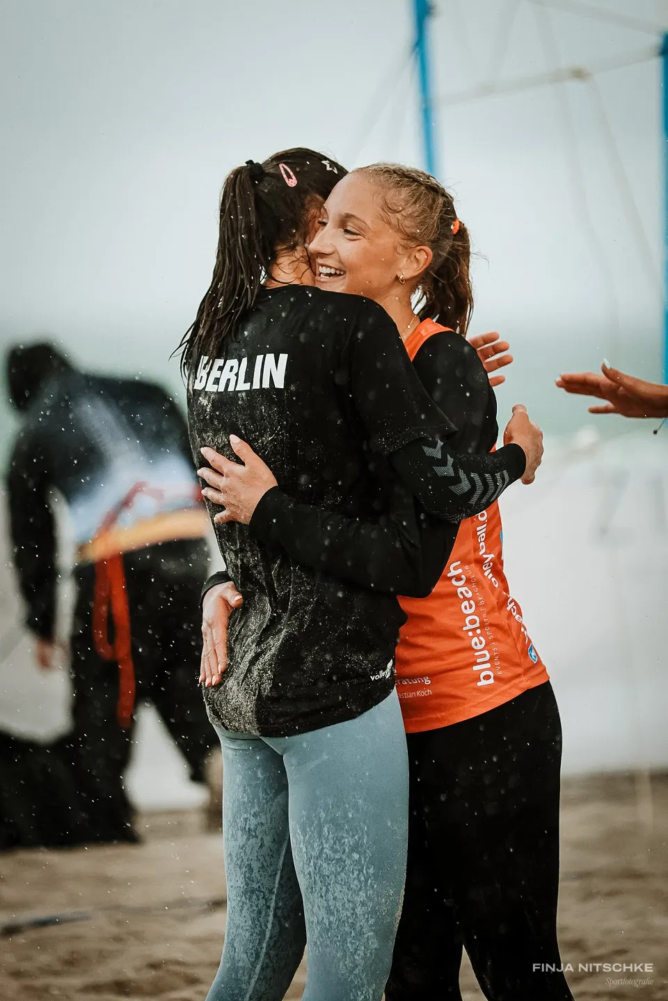 Two beach volleyball players hugging and laughing in the rain