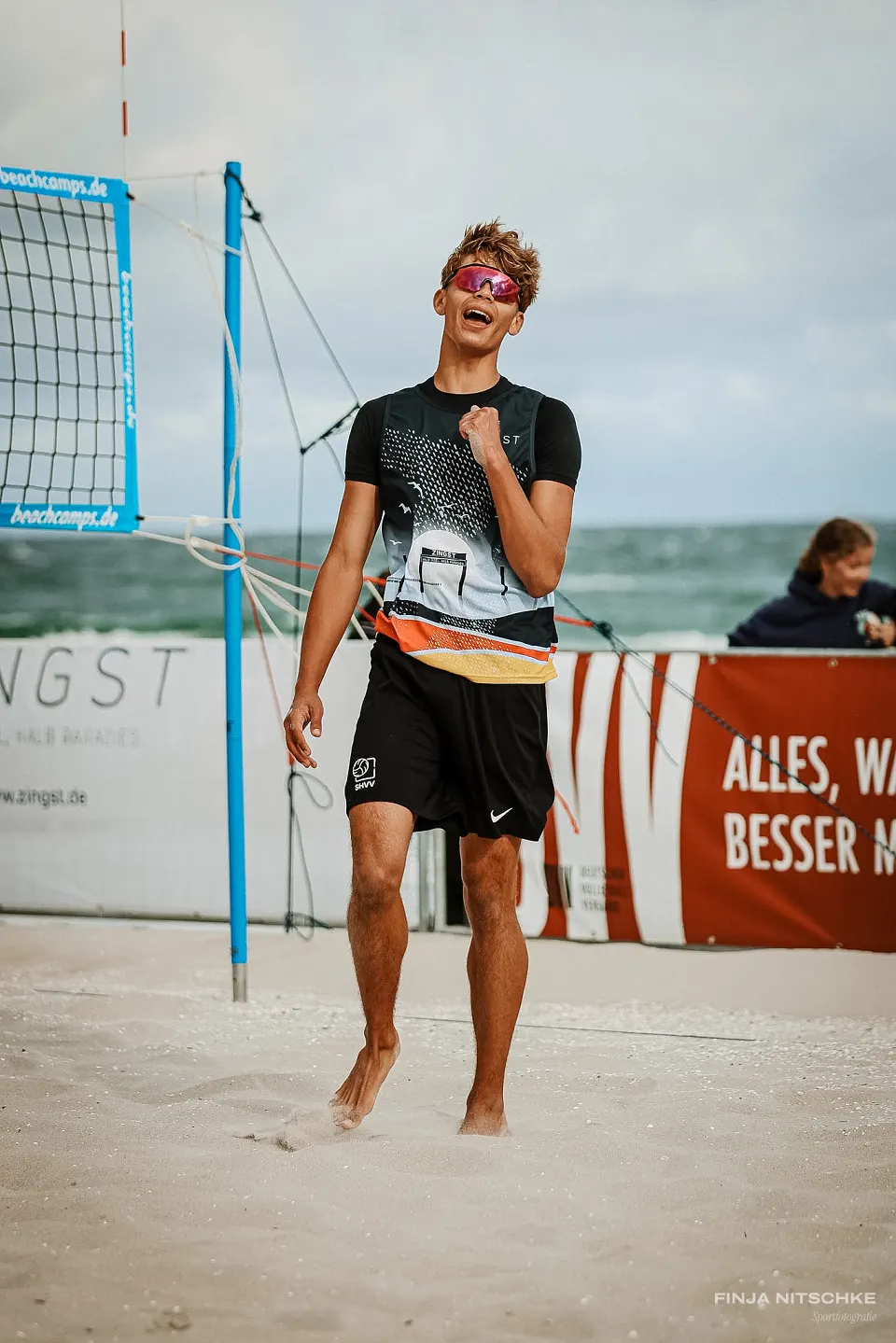 Beachvolleyballer läuft lachend über den Sand, das Meer im Hintergrund