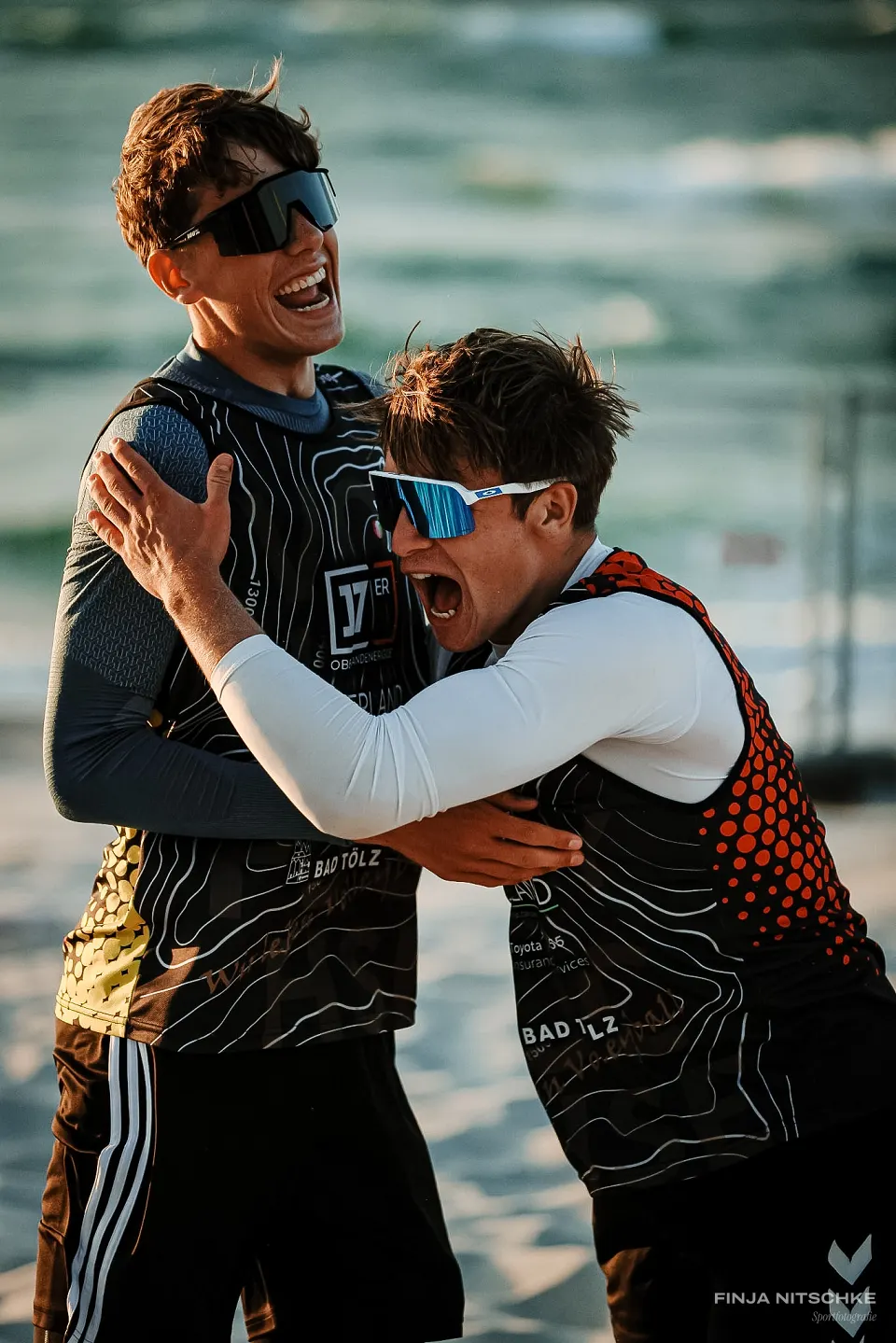 Zwei Beachvolleyballer umarmen sich jubelnd im Abendlicht